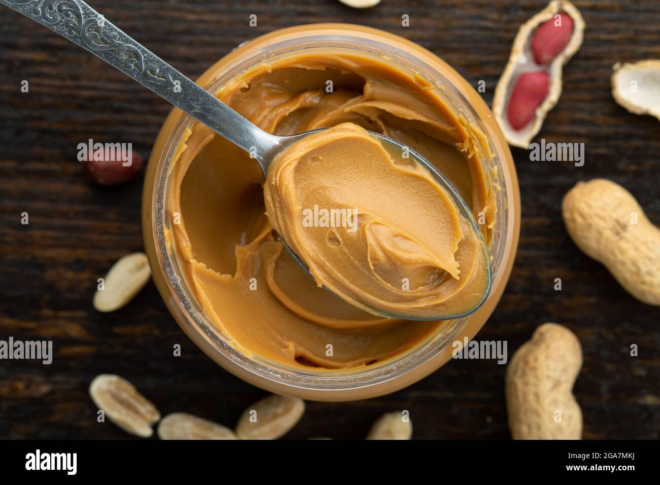 Peanut butter in an open jar and peanuts in the skin are scattered on