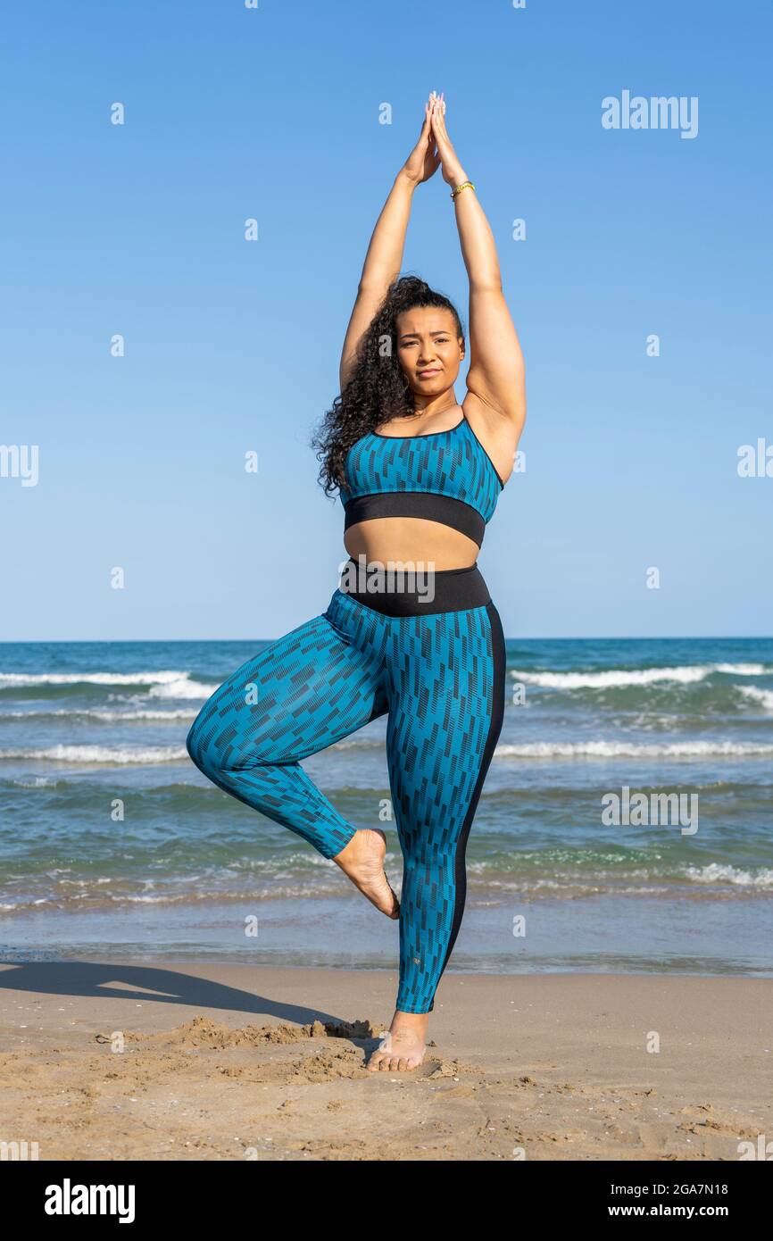 Beautiful plus size woman practicing yoga ,tree pose with namaste on beach  Stock Photo - Alamy