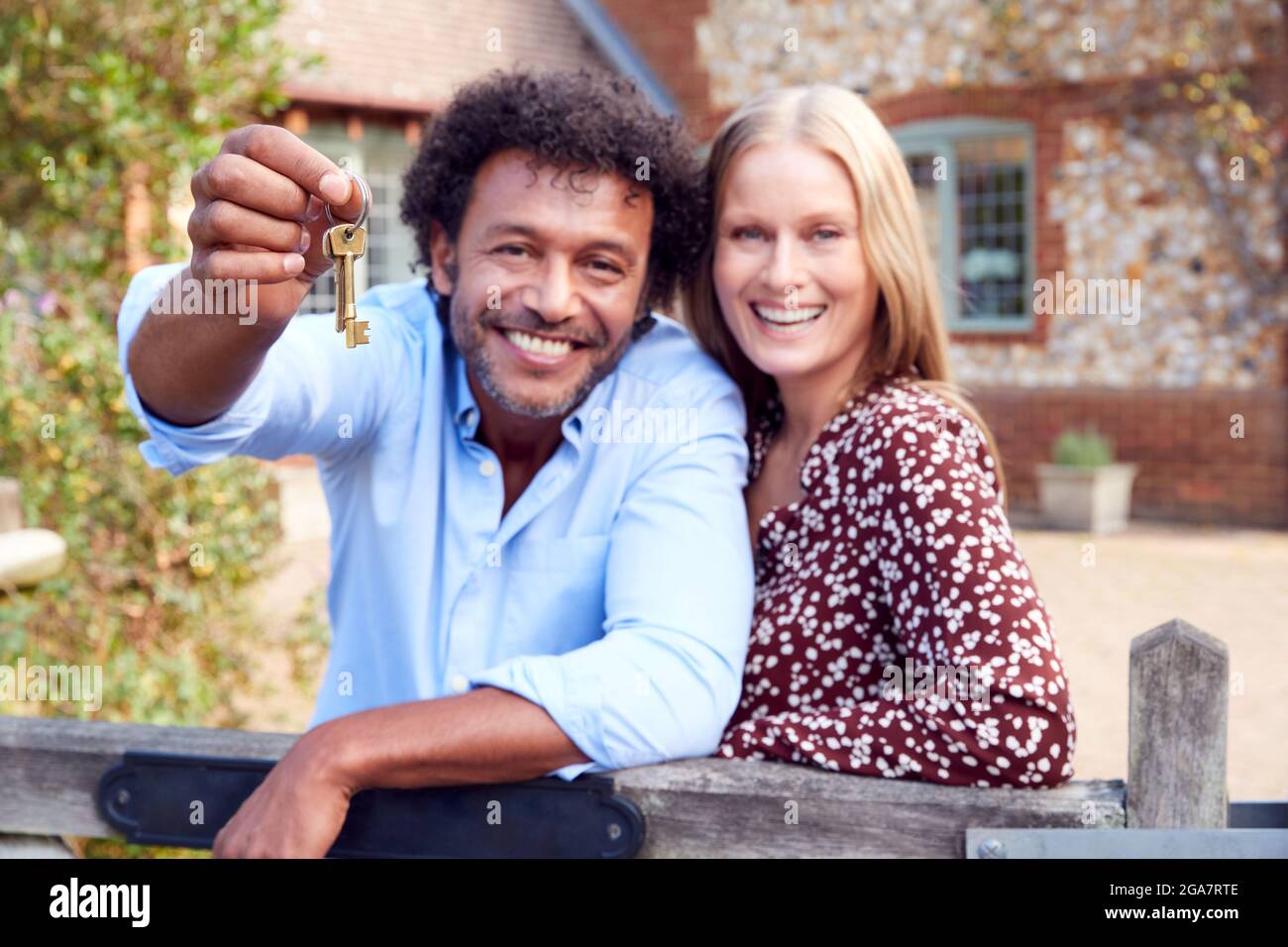Portrait Of Excited Couple By Gate Holding House Keys Outside New Home ...