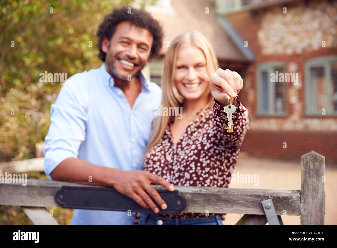 Portrait Of Excited Couple By Gate Holding House Keys Outside New Home ...