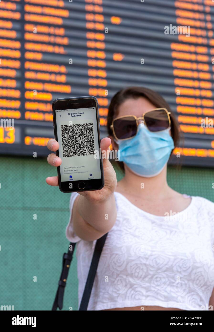 Rome, Italy. 29th July, 2021. Rome, Italy, Thursday July 29th 2021. Young woman travelling on Italian railways holds up a Covid Green pass digital certificate in front of a train timetable notice. Stock Photo