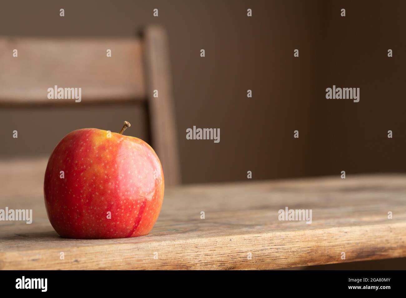 single red apple close up, sitting on vintage wood school desk with copy space on neutral background and natural lighting Stock Photo