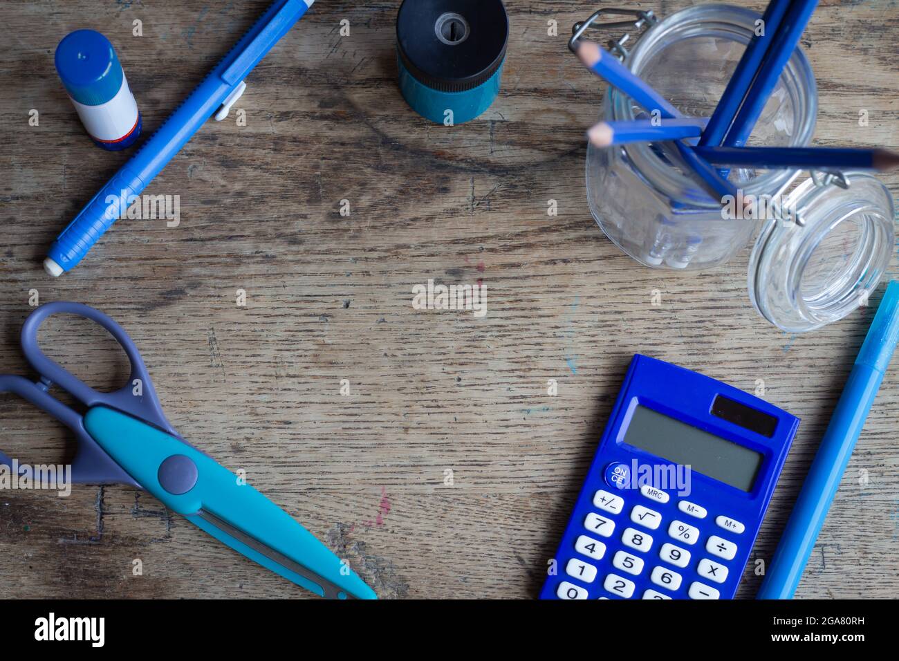 blue coloured school supplies on vintage wood desk top, including scissors, calculator, pencils, glue eraser and pencil sharpener, with copy space Stock Photo