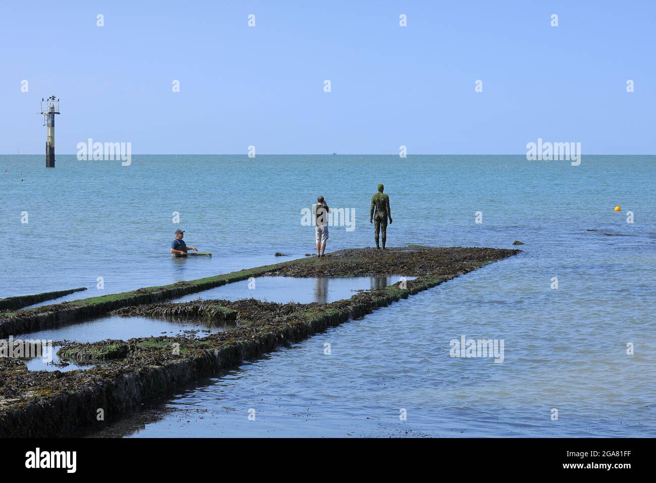 A man photographs the Antony Gormley statue Another Time while a fisherman in the sea looks on