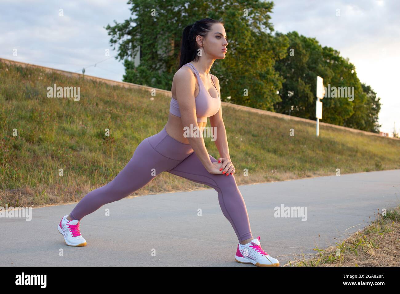 Young Caucasian woman doing lunge warm up exercise at embankment before running Stock Photo