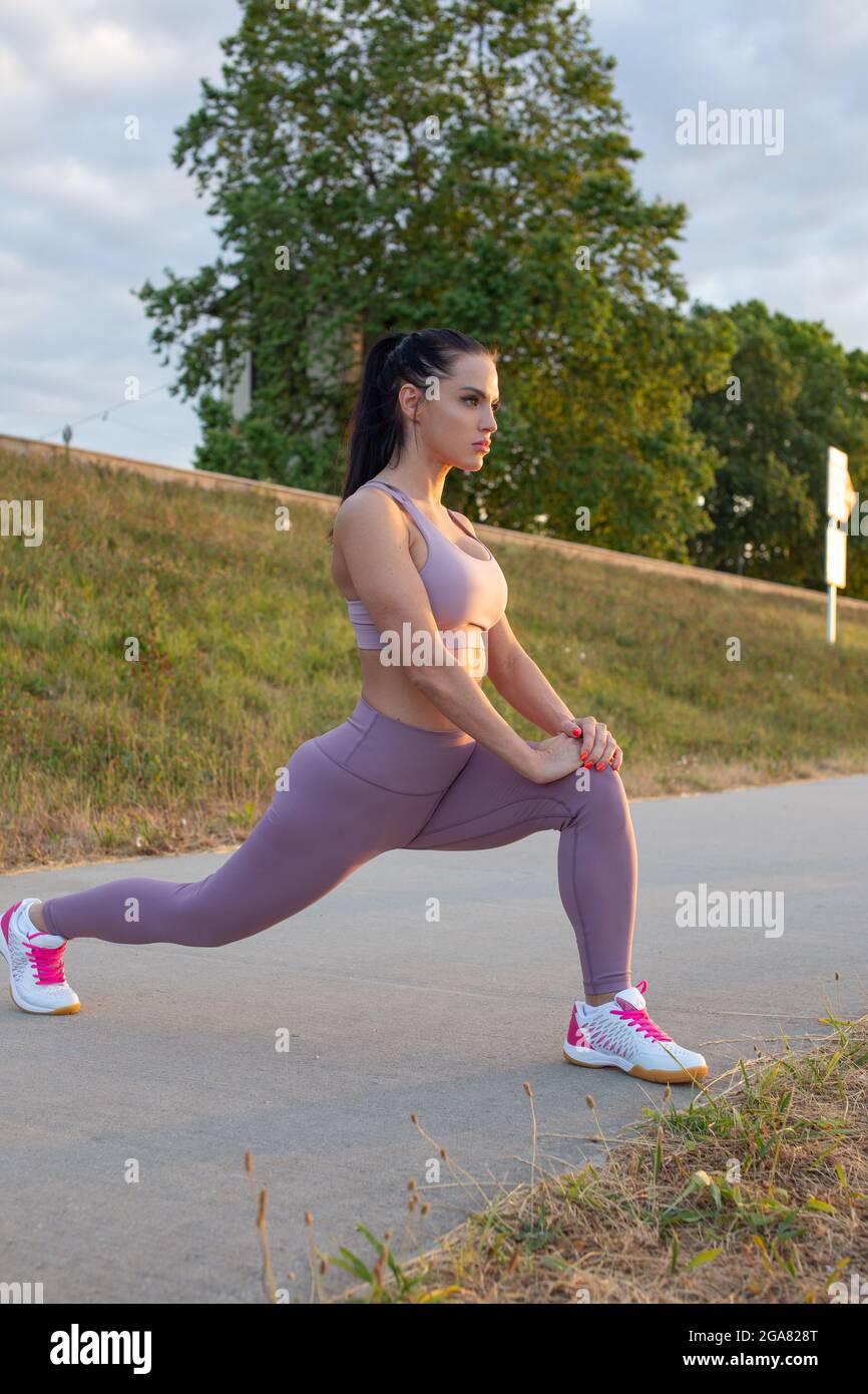 Young woman stretching before running at embankment, warm up exercise Stock Photo