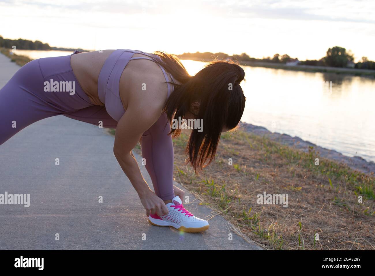 Woman in sportswear adjusting shoes before running at riverside Stock Photo