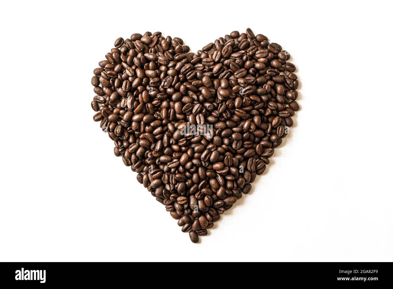 Coffee beans in shape of heart. A macro photo of fried brown coffee beans on the white table. Stock Photo