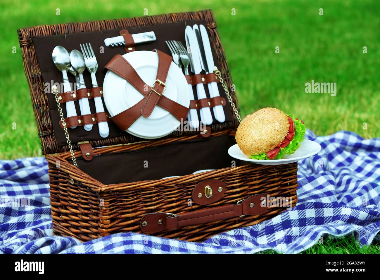 Wicker picnic basket, tasty sandwiches and plaid on green grass ...