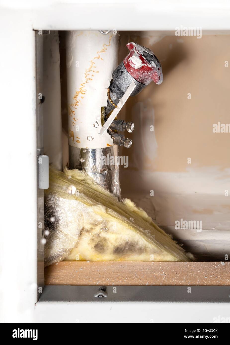 Dripping water from a pipe next to a water shut-off valve from a ceiling hatch in building corridor. Active leak. Cause is a pinhole leak in copper pi Stock Photo