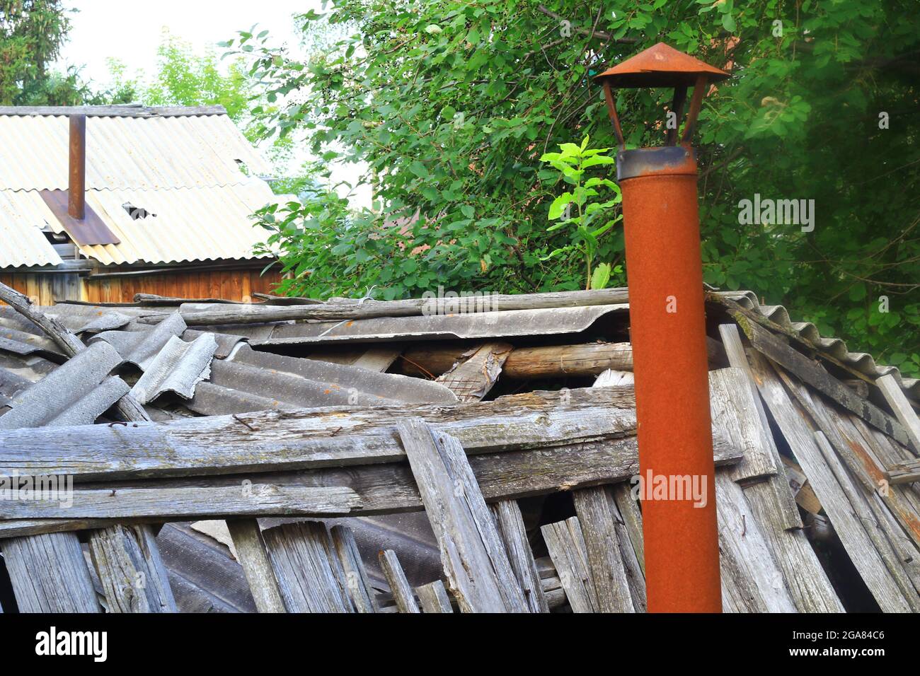 broken wooden fence of old boards with a rusty chimney Stock Photo