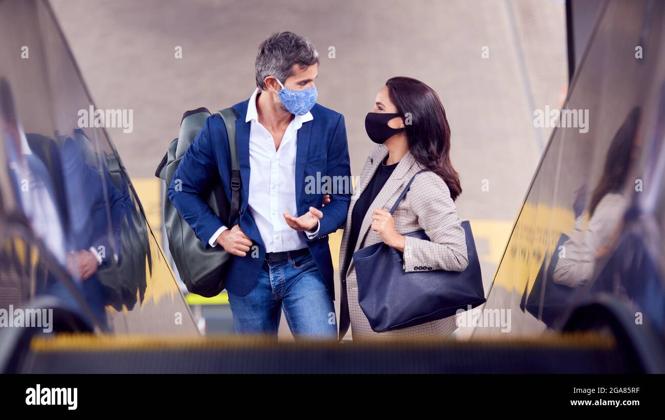 Business Couple Commuting Riding Escalator At Railway Station Wearing PPE Face Masks In Pandemic Stock Photo