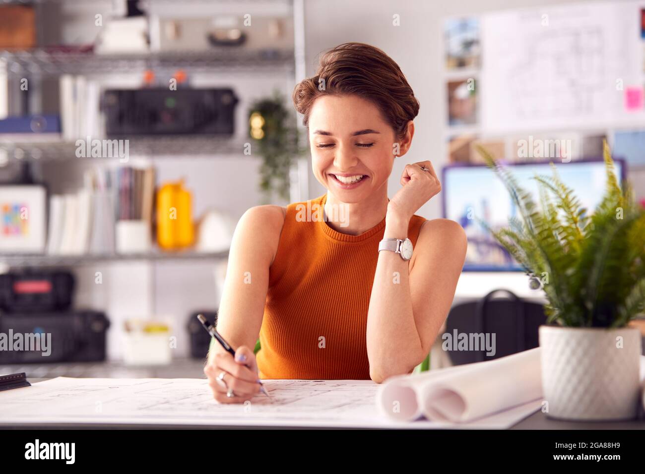Female Architect In Office Working At Desk Making Notes On Plan Or Blueprint Stock Photo