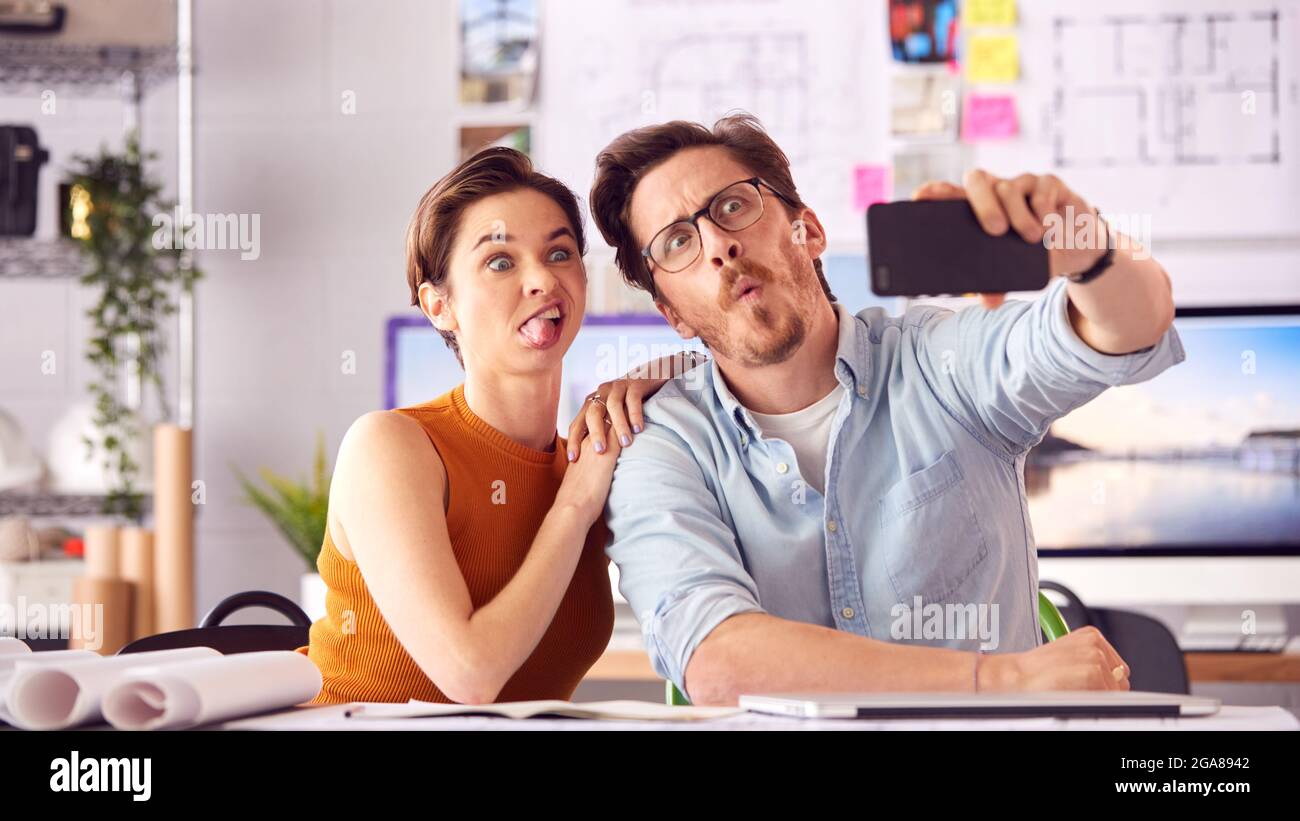 Male And Female Architects In Office Posing For Selfie And Pulling Funny Faces Together Stock Photo