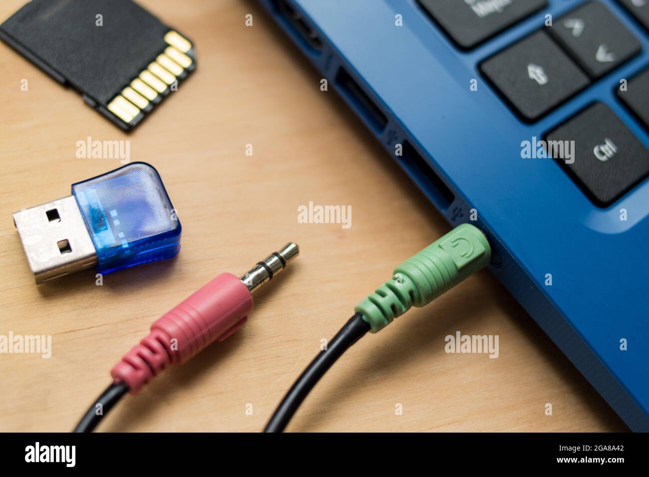 Earphones cables connected to a blue modern laptop, USB memory  and SD memory on a wooden table Stock Photo