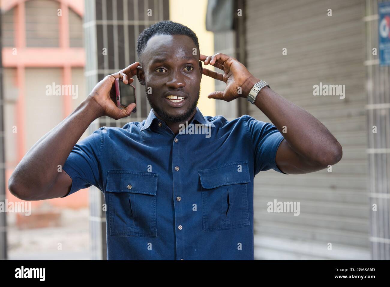 surprised man holds a cell phone in hand holds his ears while listening to a sound outside Stock Photo