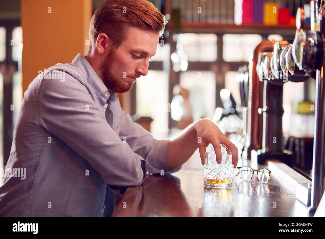 Unhappy Man Sitting At Pub Bar Drinking Alone With Glass Of Whisky Stock Photo