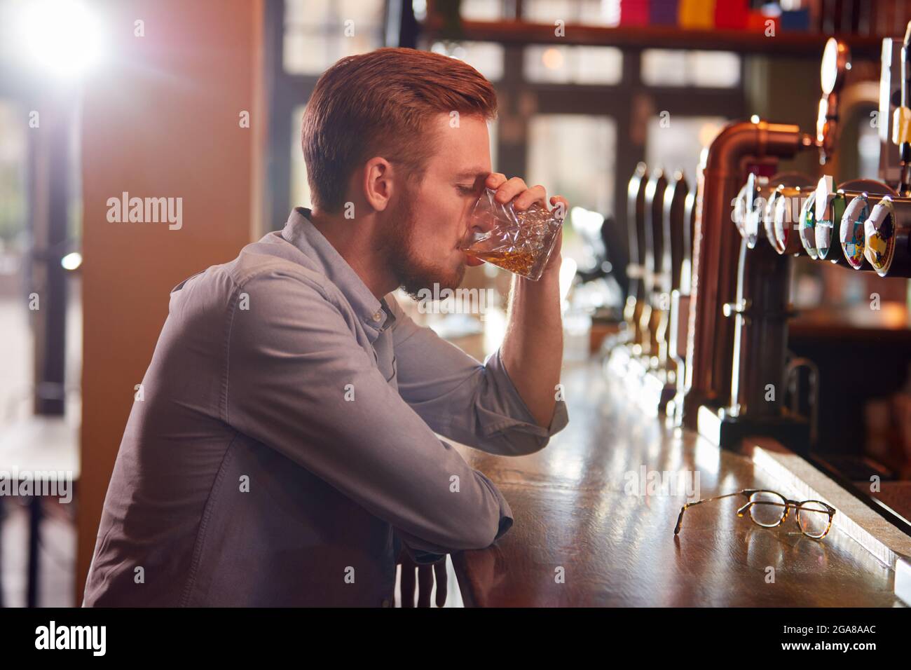 Unhappy Man Sitting At Pub Bar Drinking Alone With Glass Of Whisky Stock Photo
