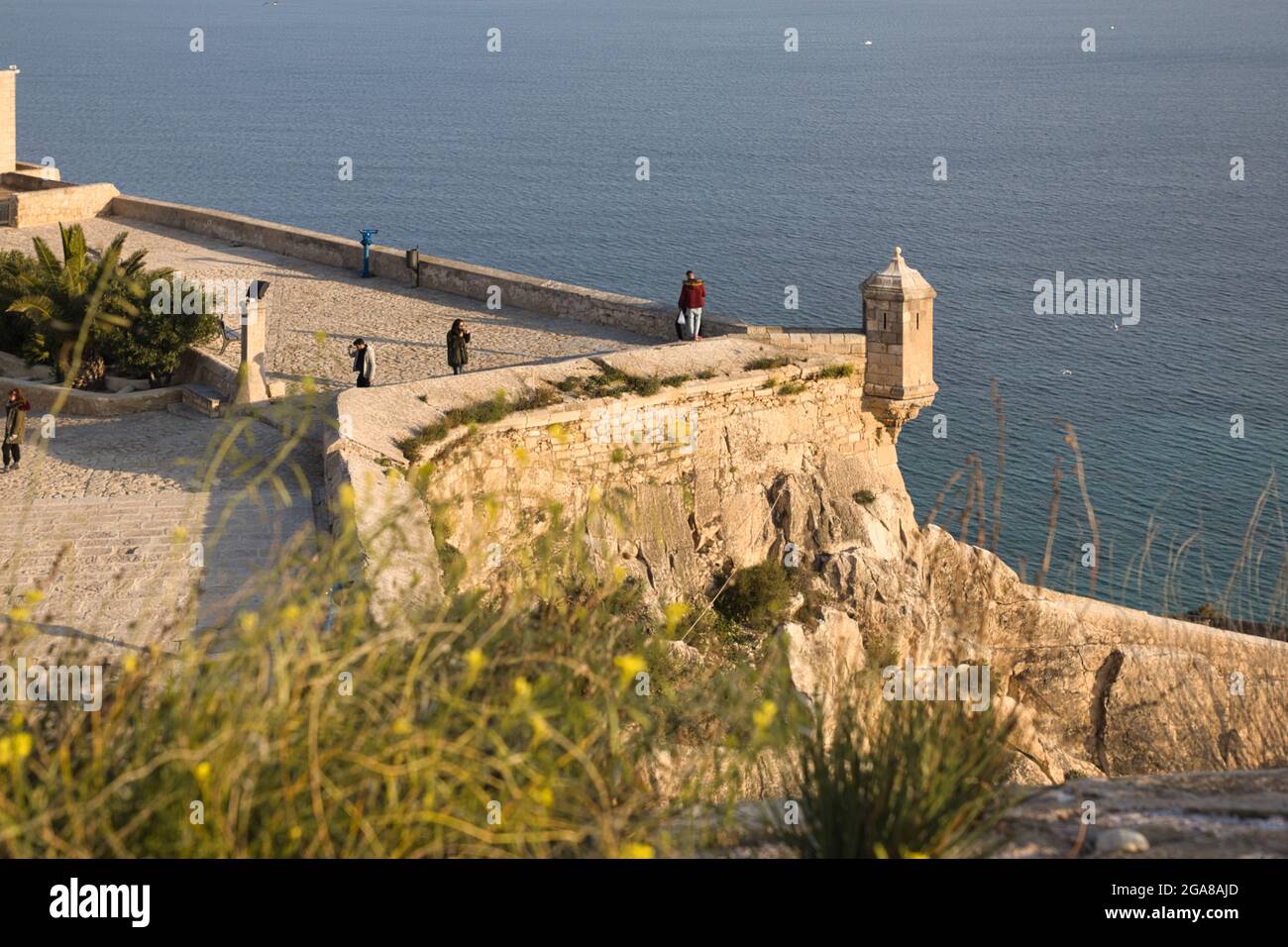 A view across the top of the castle walls of Santa Barbara castle with the Mediterranean Sea beyond, at Alicante, Spain. People sight seeing Stock Photo