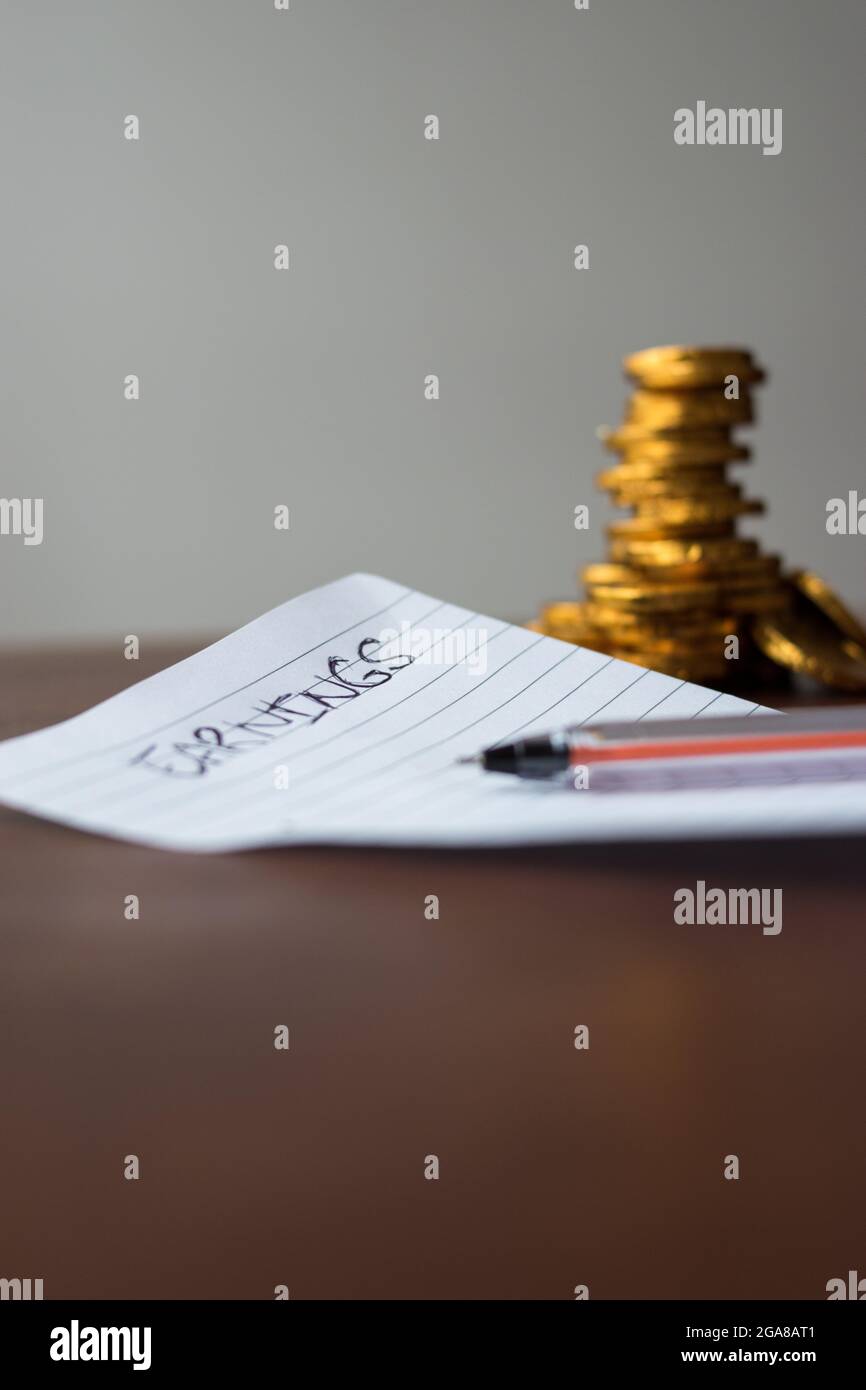 Some golden coins with an earnings list on a sheet of paper  and a black pen on a wooden table Stock Photo