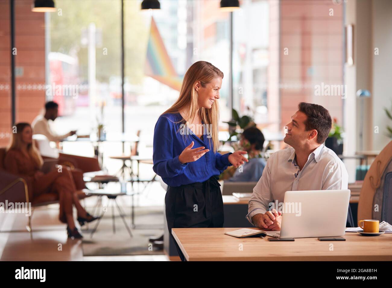 Businessman And Businesswoman Having Informal Meeting By Desk In Modern ...