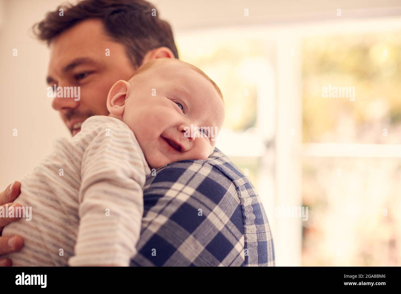 Loving Father Cuddling Baby Son Resting Over Shoulder At Home Together Stock Photo