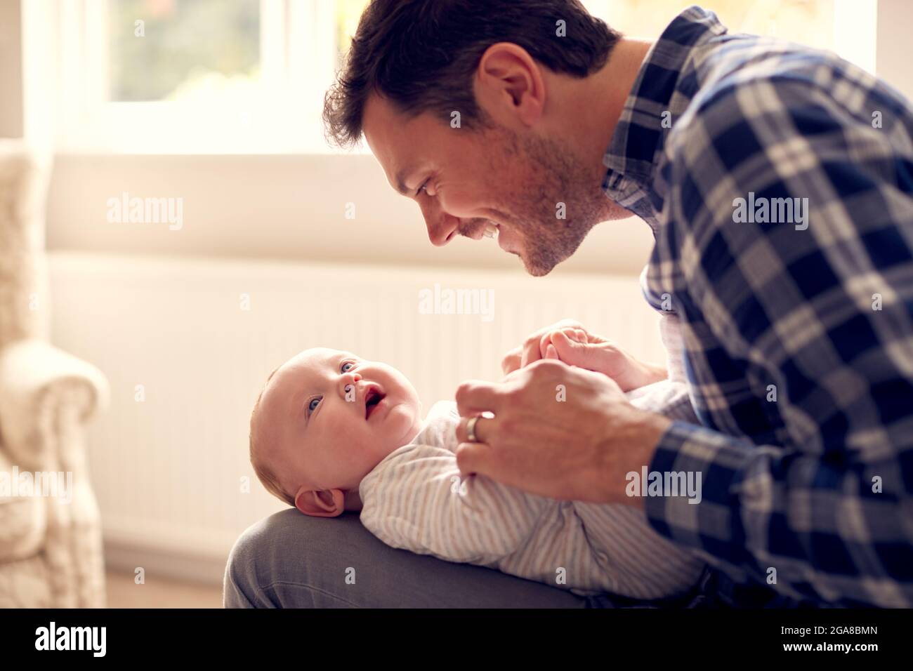 Loving Father Playing Game With Baby Son Lying On Lap At Home Together Stock Photo