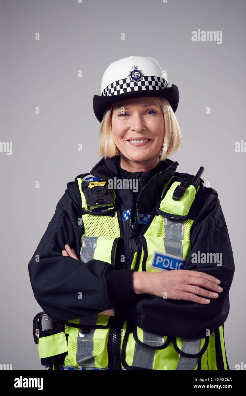 Studio Portrait Of Smiling Mature Female Police Officer Against Plain 