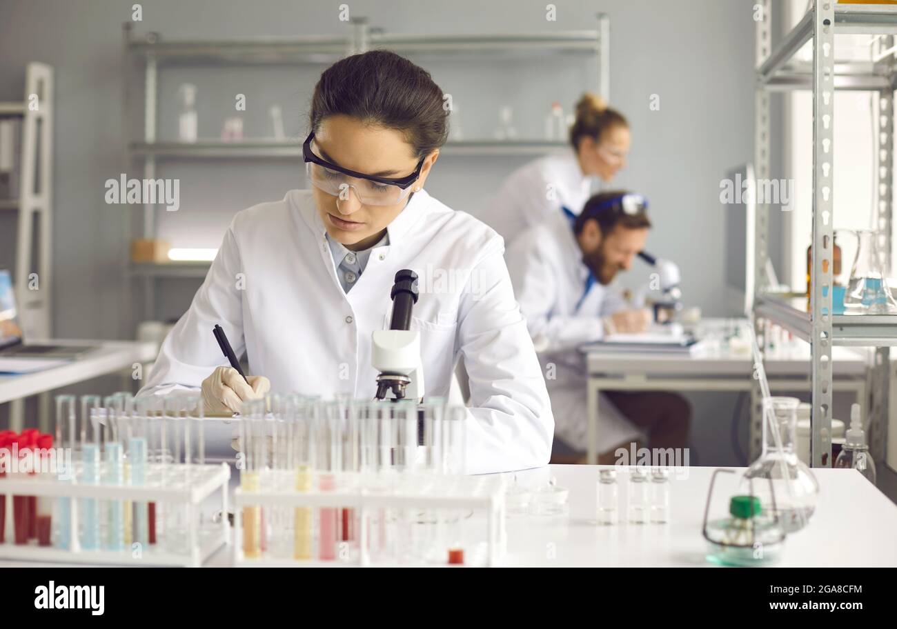 Portrait of young serious female scientist making notes sitting at lab desk Stock Photo