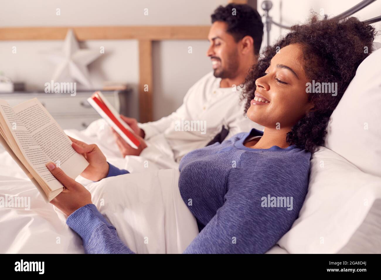 Couple In Wearing Pyjamas Lying In Bed Reading Books Together Stock Photo