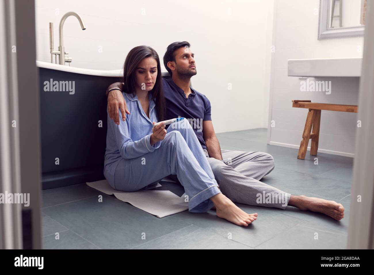 Disappointed Couple Sitting On Floor In Bathroom At Home With Negative