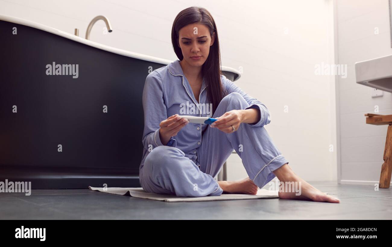 Disappointed Woman Sitting On Floor In Bathroom At Home With Negative