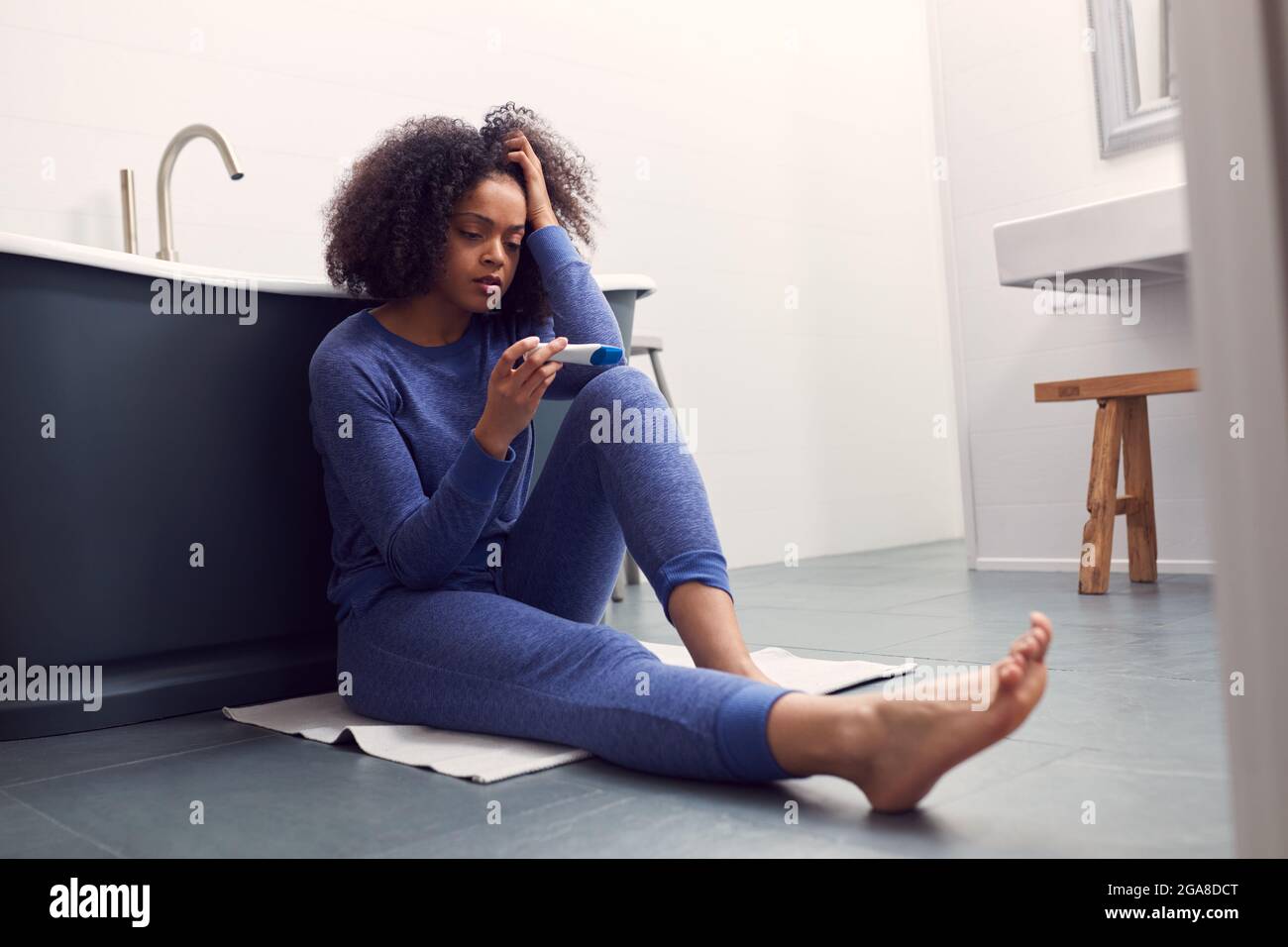 Disappointed Woman Sitting On Floor In Bathroom At Home With Negative