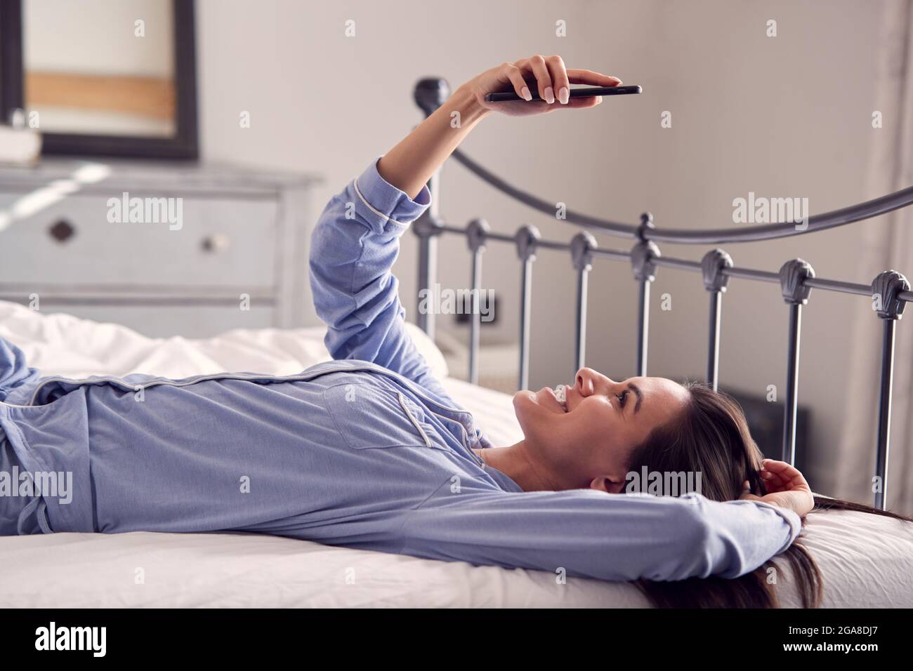 Woman Wearing Pyjamas Taking Selfie On Mobile Phone Lying On Bed Stock  Photo - Alamy