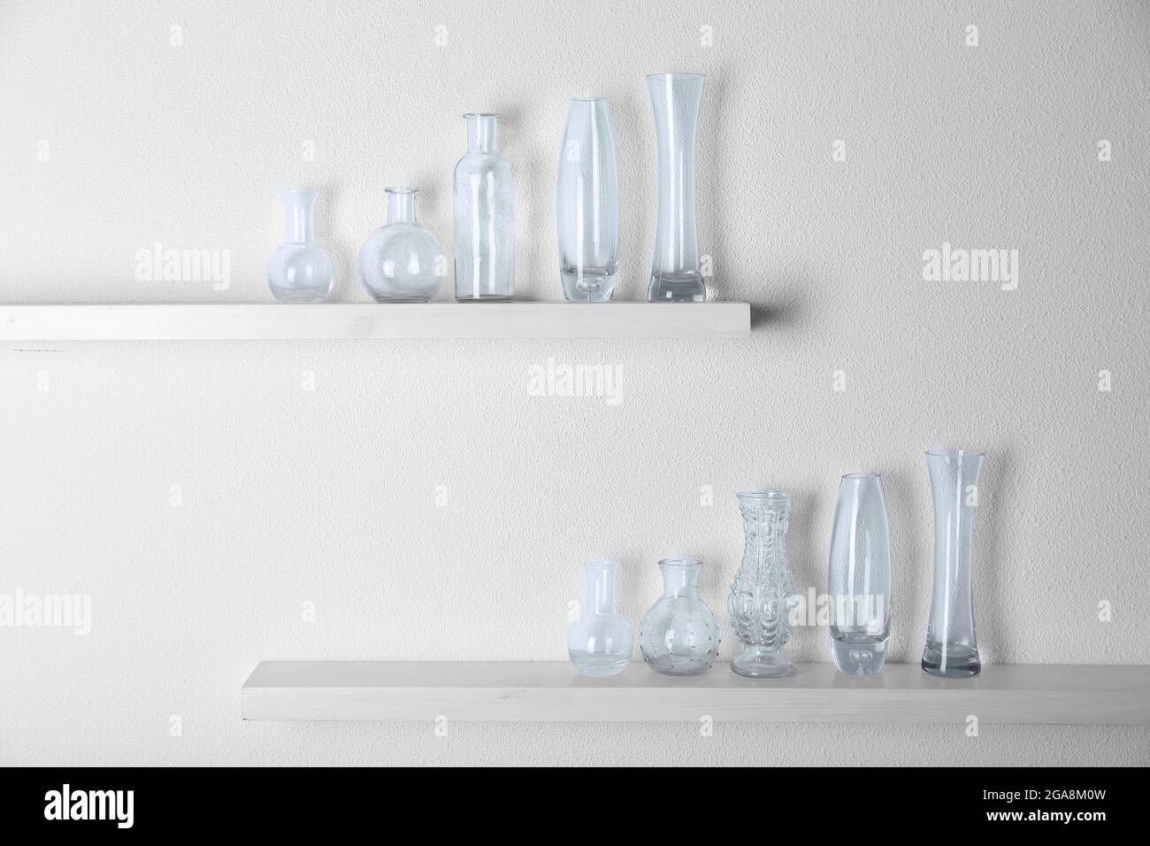 Decorative glass vases on wooden shelf on white wallpaper background