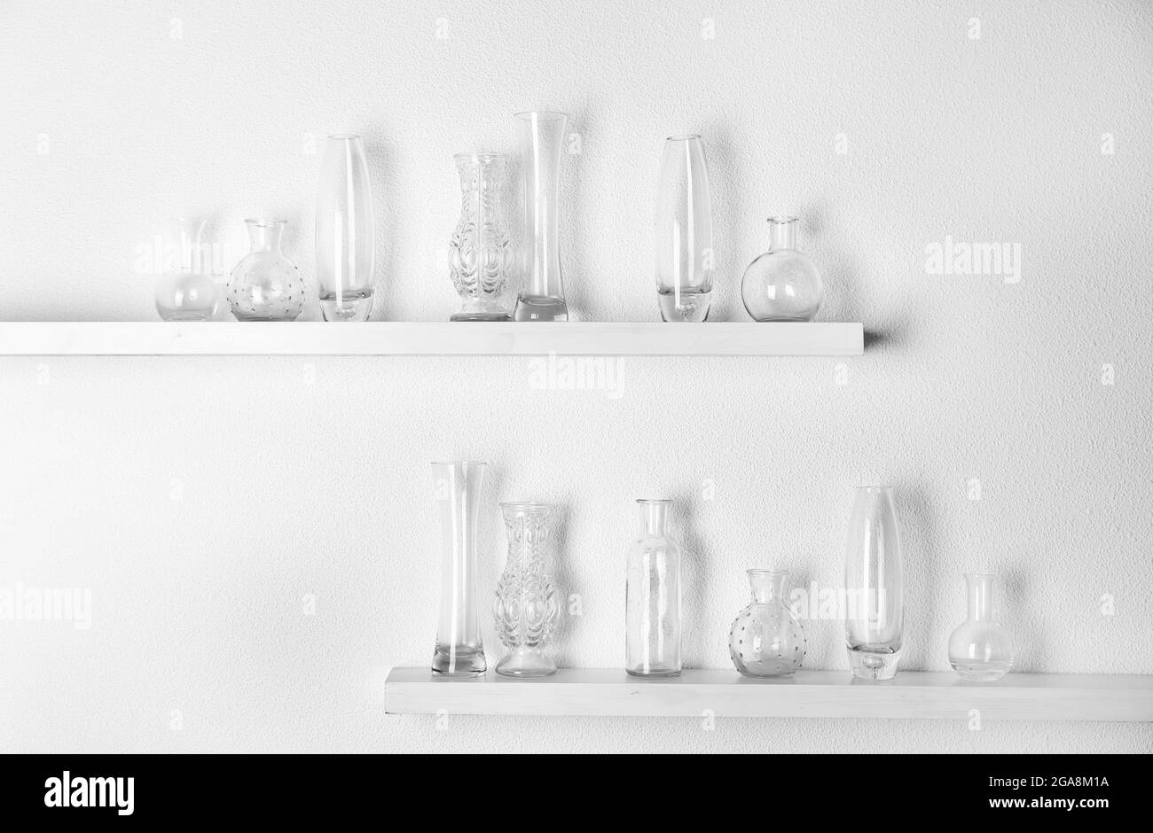 Decorative glass vases on wooden shelf on white wallpaper background