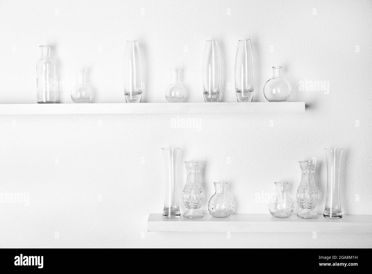 Decorative glass vases on wooden shelf on white wallpaper background