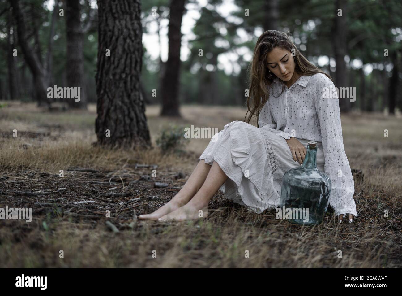 Spanish barefoot woman in a white dress sitting on a tree stump with a ...