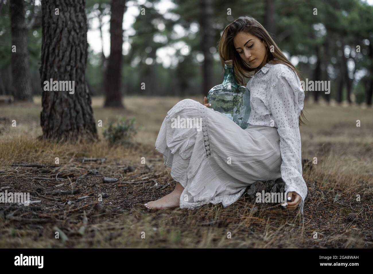 Spanish barefoot woman wearing a white dress and holding a glass jug