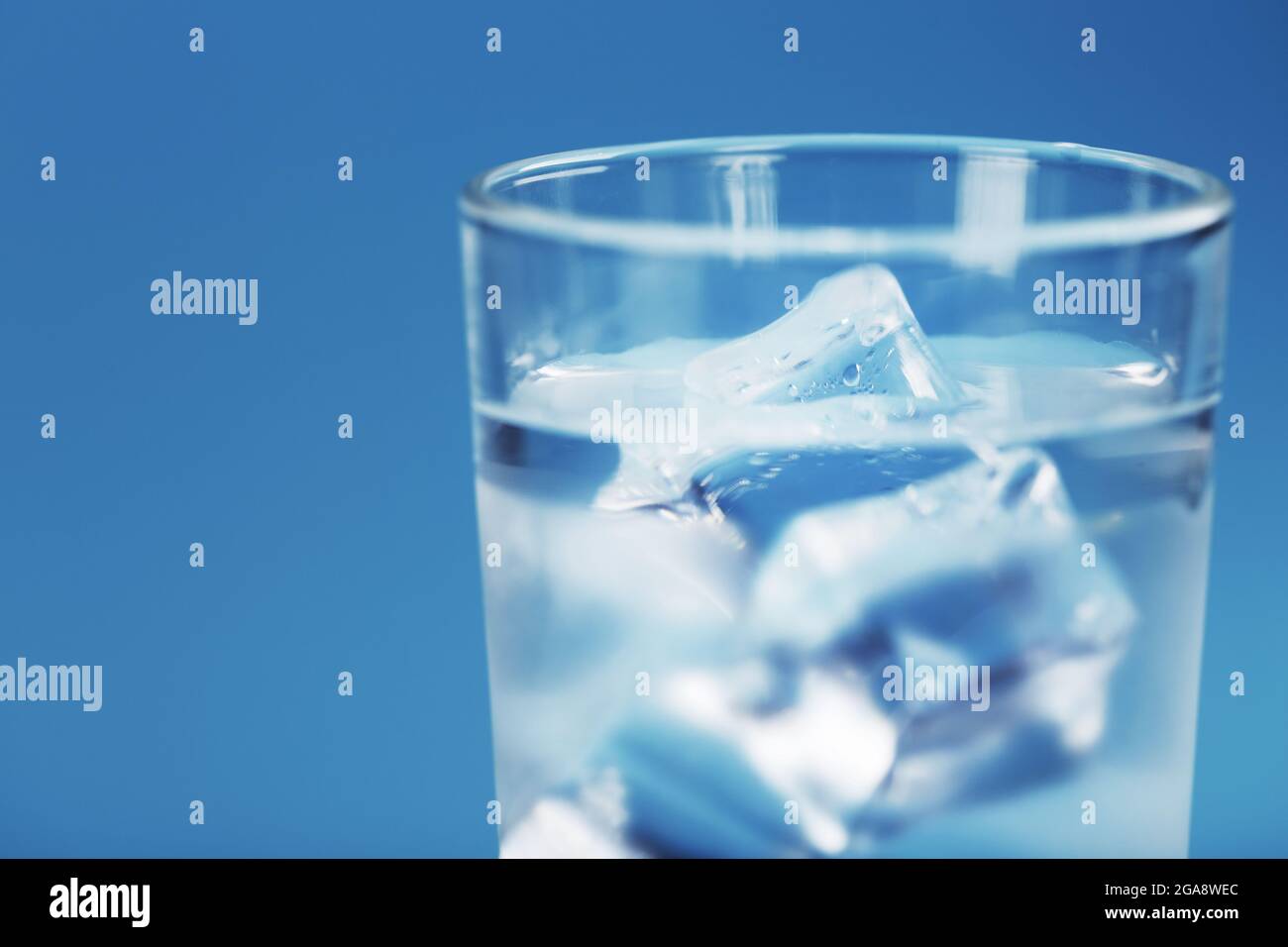A glass with ice water and ice cubes on a blue background. A refreshing ...
