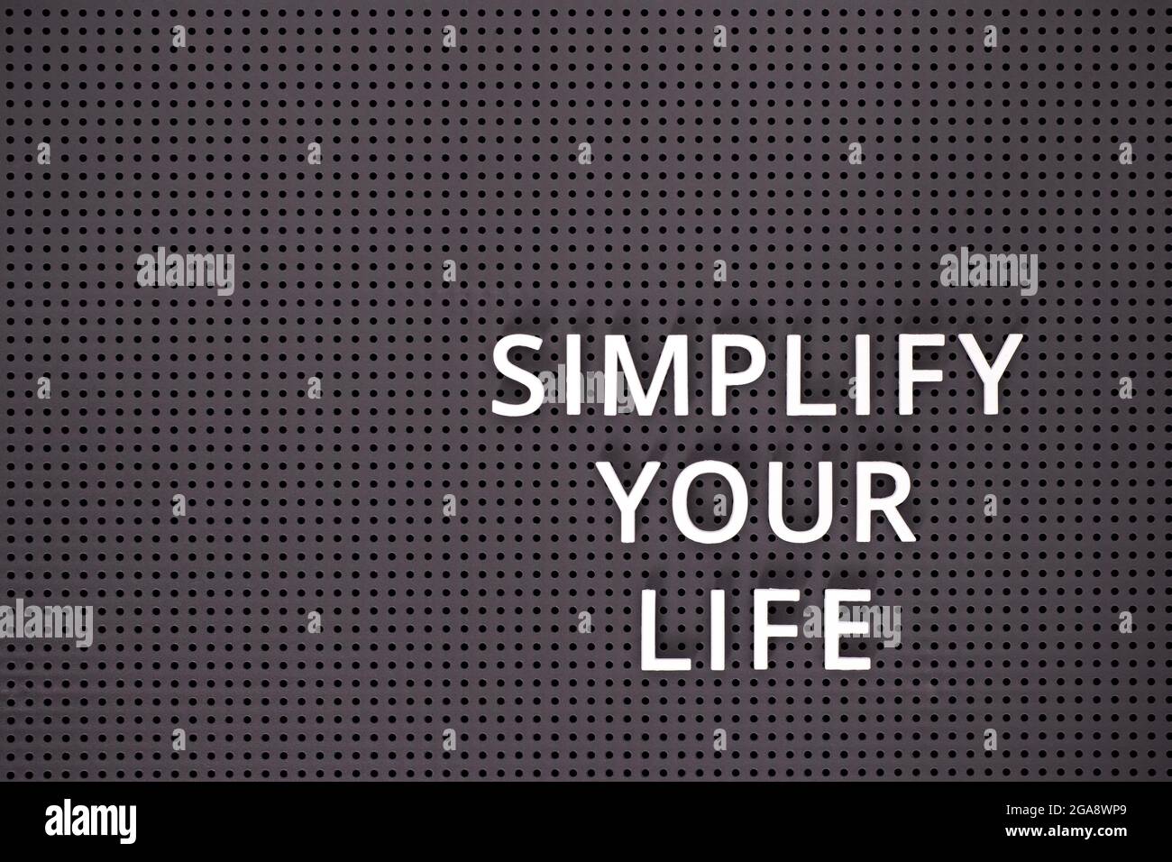 Phrase Simplify Your Life spelled out with white letters on a gray pegboard Stock Photo