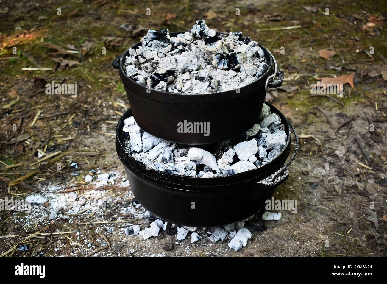 Two cast iron dutch ovens stacked on top of each other baking. They are covered in charcoal. Stock Photo