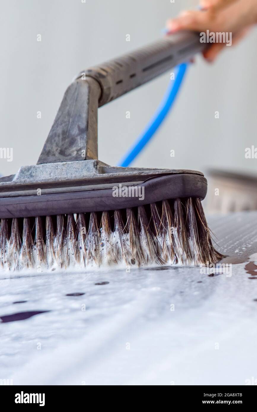 The woman washes the car. A woman at a car wash washes her car with a brush with car shampoo. To