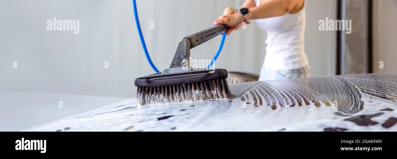 The woman washes the car. A woman at a car wash washes her car with a brush with car shampoo. To