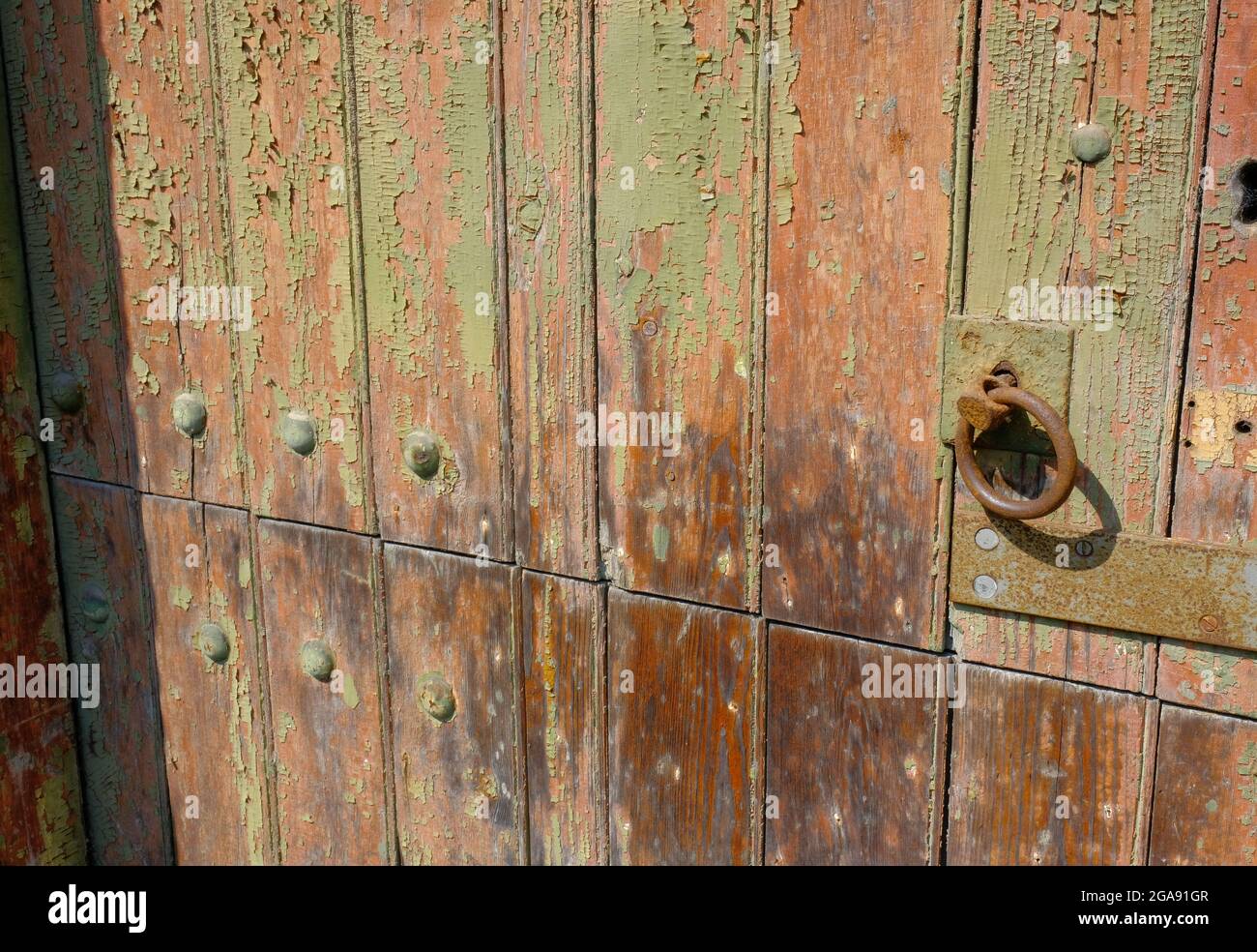 Old wooden door with flaking green paint, bolts and rusted handle. Stock Photo