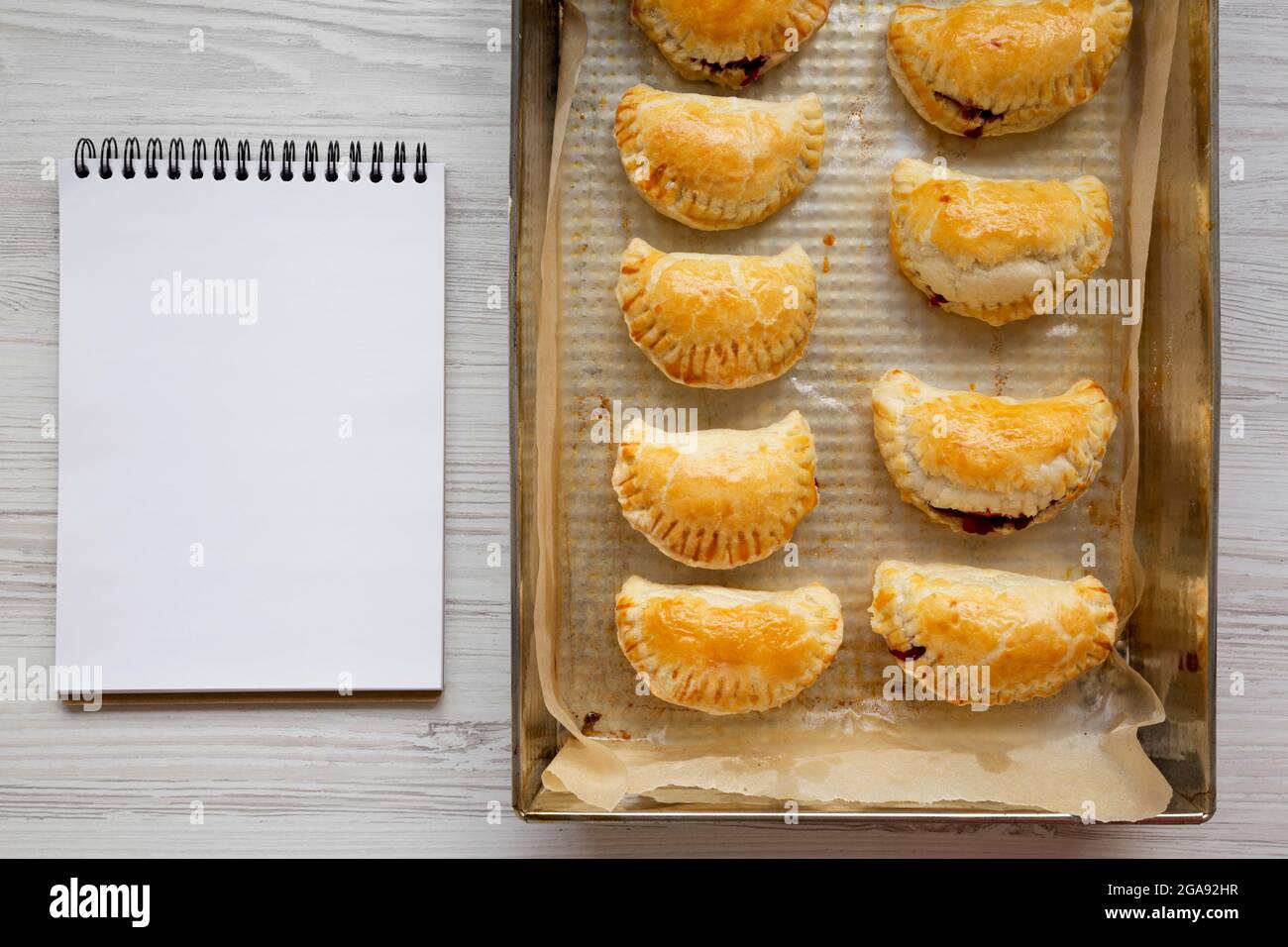 Homemade Cherry Hand Pies in a baking pan, blank notepad, top view ...