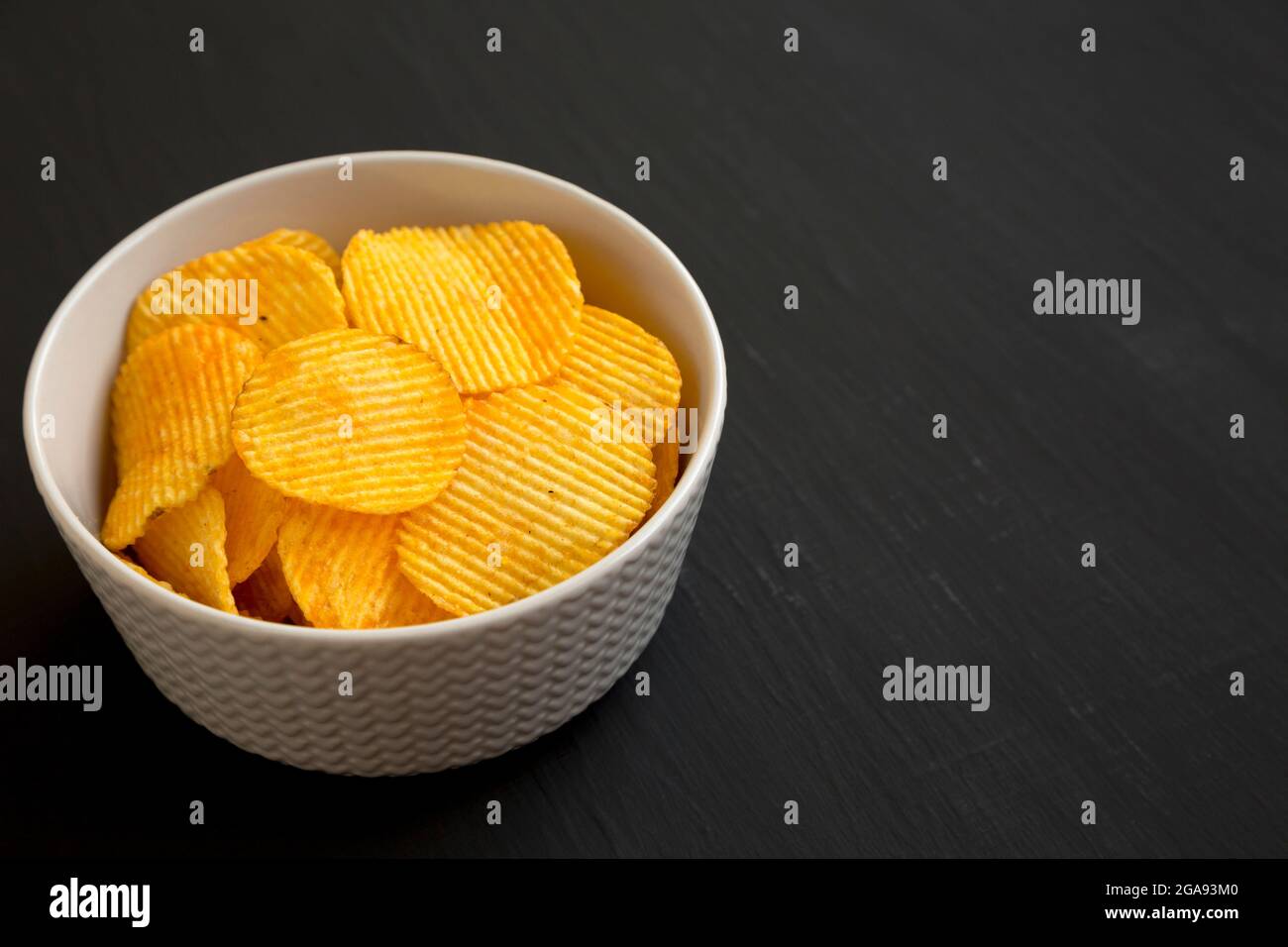 Ruffled Cheese Potato Chips in a Bowl on a black background, side view. Copy space. Stock Photo