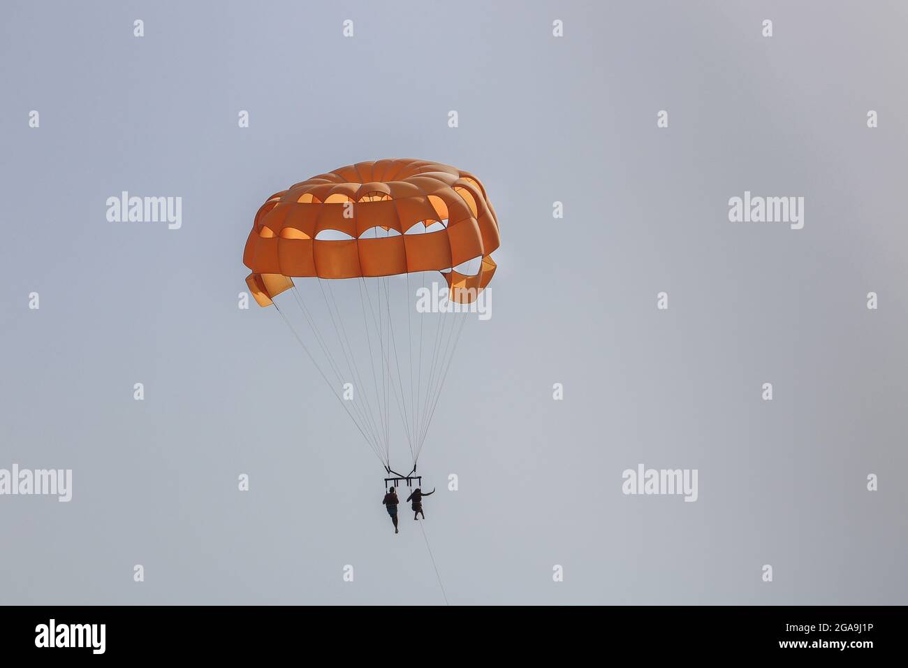 Orange Parachute High In The Sky With Two People On The Parasailing Stock Photo