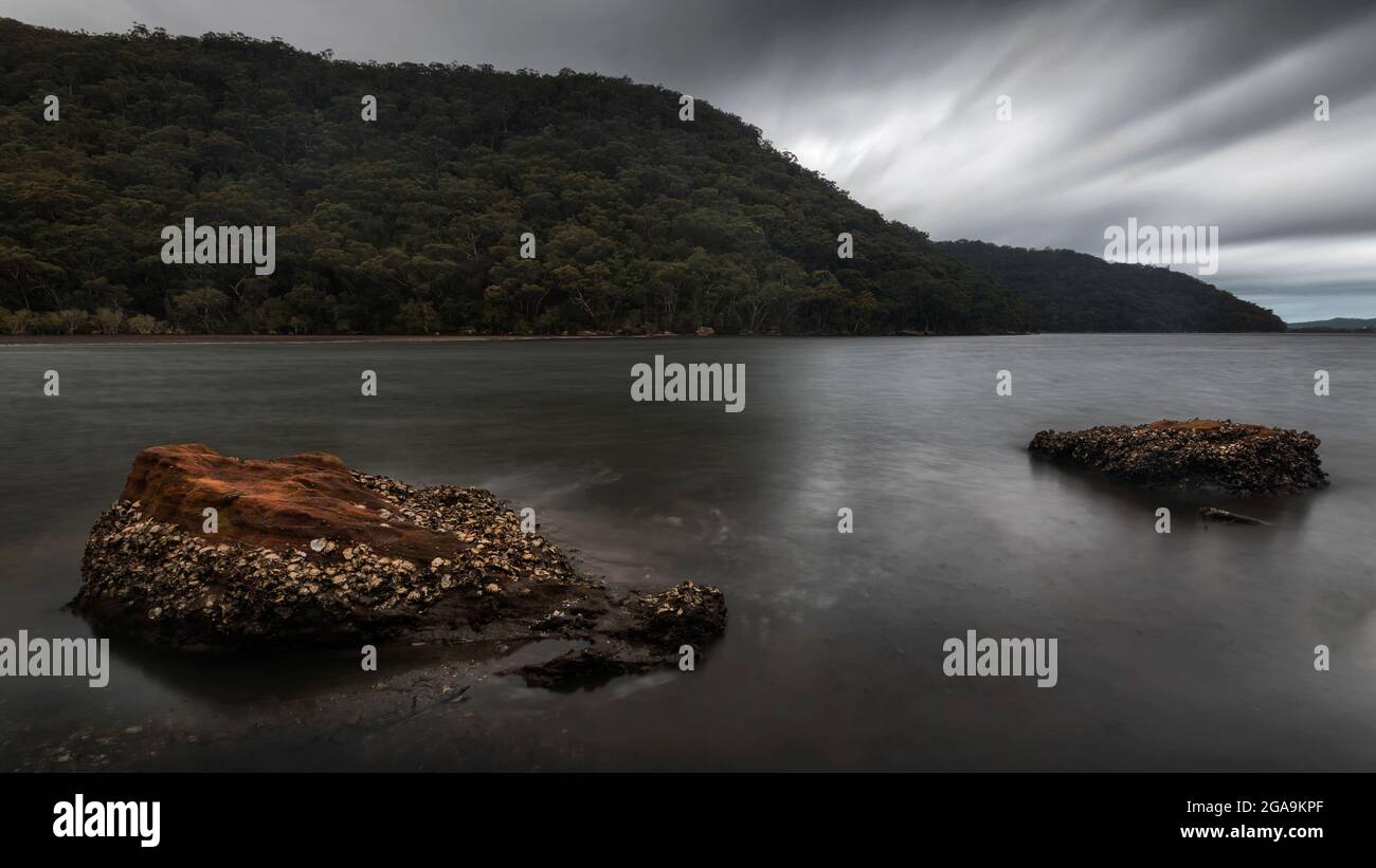 rocks in the lake under a mountain and overcast sky Stock Photo