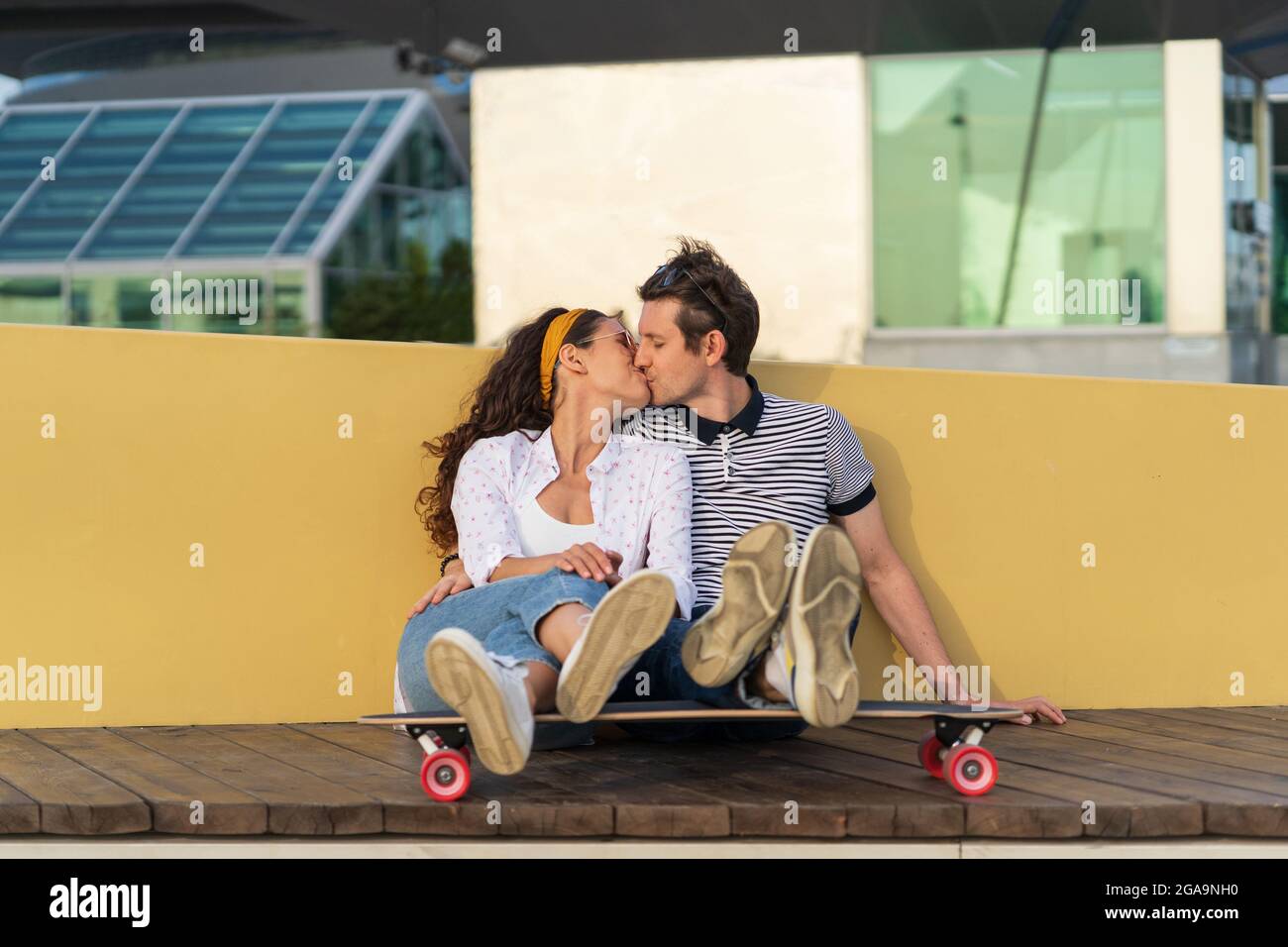 Couple of skaters kissing sit on longboard together outdoors in urban space. Youth, romance and love Stock Photo